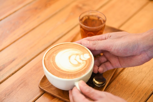 Koffiekopje in de hand op houten tafel in café, geserveerd koffie cappuccino of latte en thee