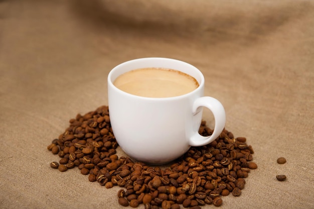 Koffiekopje met geroosterde bonen Cappuccino met melk witte mok koffiebonen bruine stof achtergrond