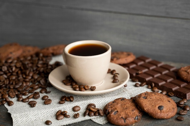 Koffiekopje met koekjes en chocolade met verspreide koffiebonen op linnen en houten tafel