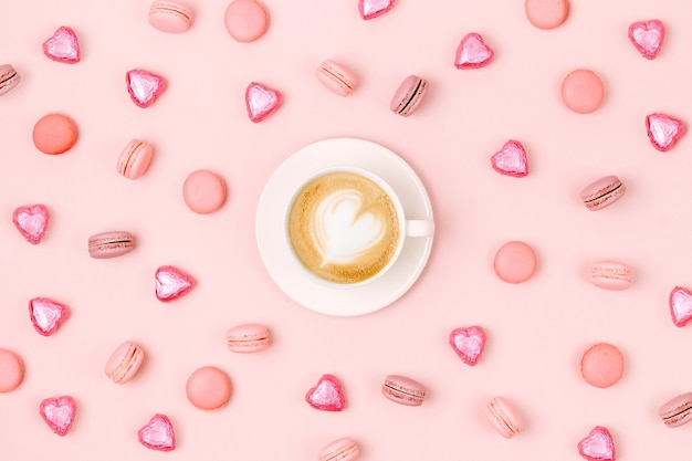 Koffiekopje met snoep en bitterkoekjes op lichtroze achtergrond. Platliggend, bovenaanzicht