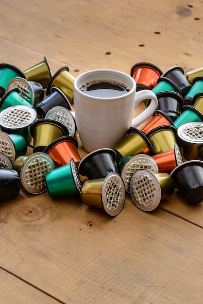 Koffiekopje omgeven door gebruikte koffiecapsules op houten tafel