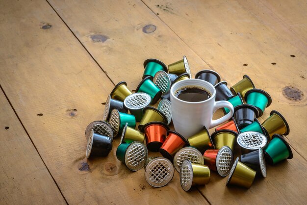 Koffiekopje omgeven door gebruikte koffiecapsules op houten tafel