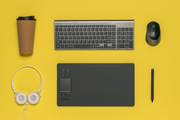 Koffiekopje, toetsenbord, muis en grafisch tablet op geel