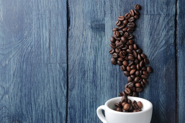 Koffiekopje voor espresso en koffiebonen in de vorm van rook op een blauwe houten tafel met ruimte voor een inscriptie