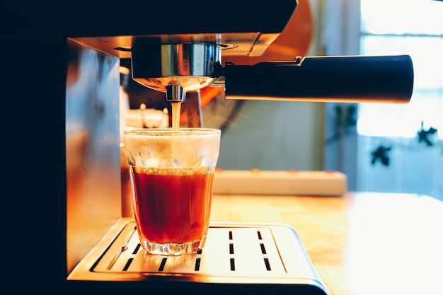 Koffiemachine giet hete zwarte thee in het glas.