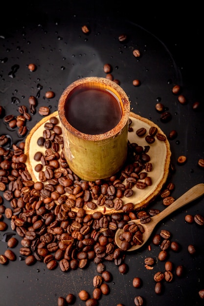 Koffiemokken gemaakt van bamboe op houten schotel en veel gebrande koffieboon verspreid op zwarte achtergrond, donkere koffie heeft rook en aroma, drankje voor pauze, ochtend- en koffietijd, lokale stijl.