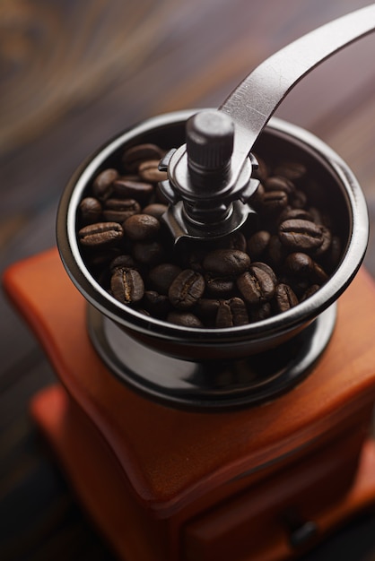 Koffiemolen op een houten tafel in een rustieke stijl. Gebrande koffiebonen in een koffiemolen. Koffie zetten om te zetten.