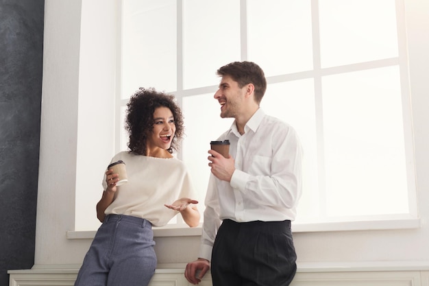 Koffiepauze. een paar jonge collega's in formele kleding die bij het raam staan en koffie drinken, leuk praten, ruimte kopiëren