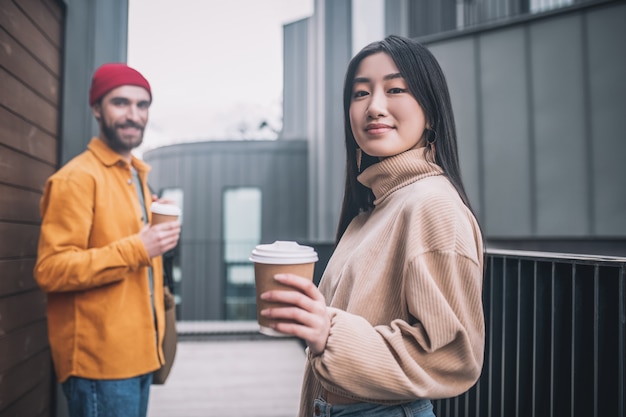 Koffiepauze. Jonge man en vrouw in vrijetijdskleding die positief kijken terwijl het hebben van koffie buiten