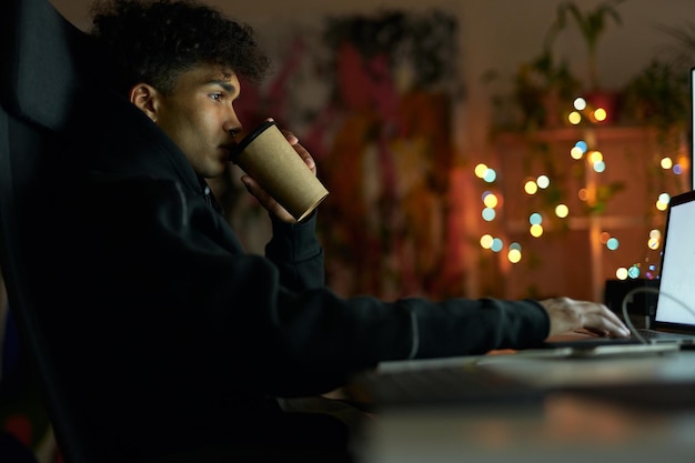 Koffiepauze zijaanzicht van jonge man met piercing koffie drinken zittend aan de tafel voor