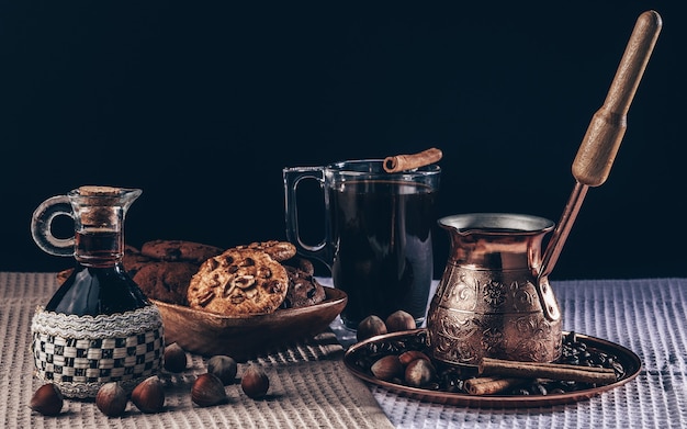 Koffiestilleven, koffie in koperen cezve met glazen beker, ontbijtkoffie met koekjes en hazelnoten