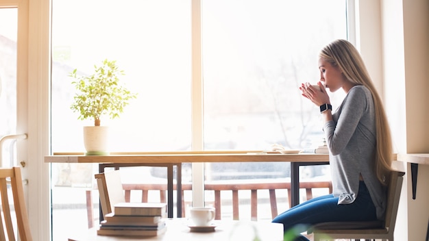 Koffietijd. Mooie jonge vrouw in café met groot raam. Vrouw koffie drinken en kijken naar raam