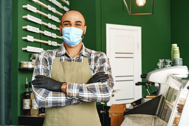 Koffiewinkelmedewerker die medisch masker draagt terwijl hij aan balie in cafetaria staat