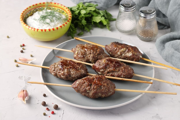 Kofta kebab on wooden skewers on a plate and sauce on the table, traditional dish of Arab cuisine, grilled minced meat shish kebab, Closeup