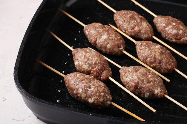 Kofta sjasliek op houten spiesjes wordt gekookt in een grillpan, bovenaanzicht, close-up