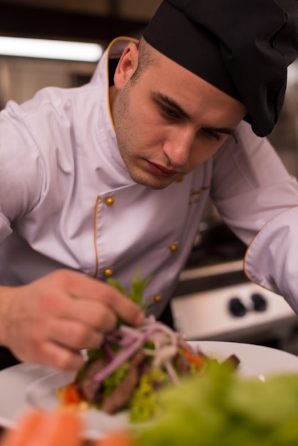 Foto kok chef-kok decoreren garnering bereide maaltijd schotel op de plaat in restaurant commerciële keuken