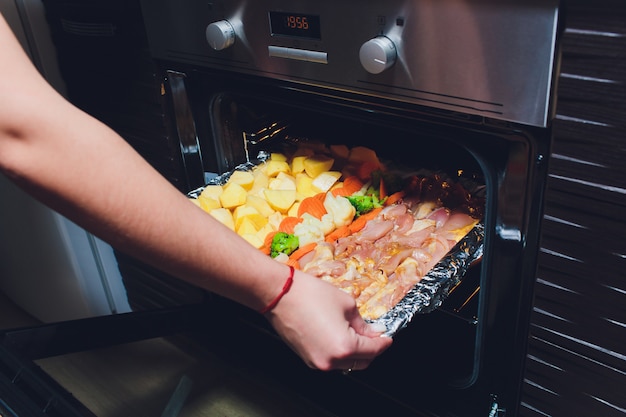 Kok die klaar gebraden gebakken kip met groenten uit de oven nemen. Thuis koken concept.