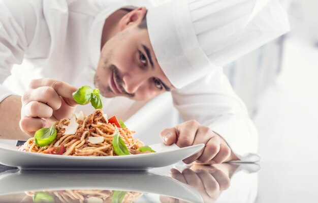 Foto kok in de keuken van een restaurant bereidt en versiert de maaltijd met de handen kok bereidt spaghetti bolognese voor