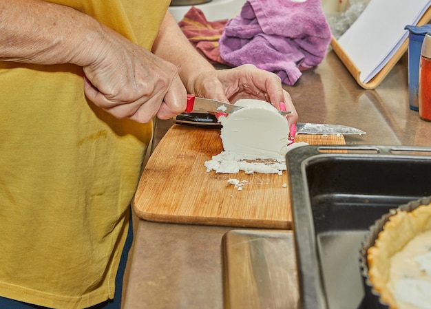 Kok snijdt de kaas met een mes op een houten plank om een taart te maken