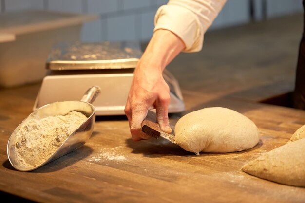 Foto koken, bakken en mensen concept - chef-kok of bakker portionering deeg met bank cutter in de bakkerij