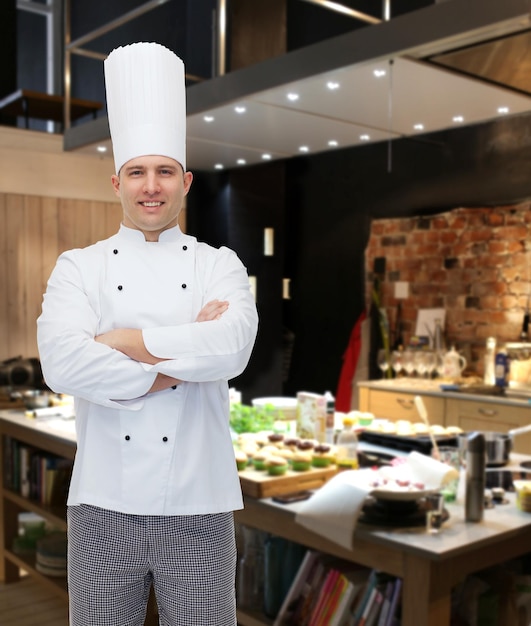 koken, beroep en mensenconcept - gelukkige mannelijke chef-kok met gekruiste handen over restaurantkeuken