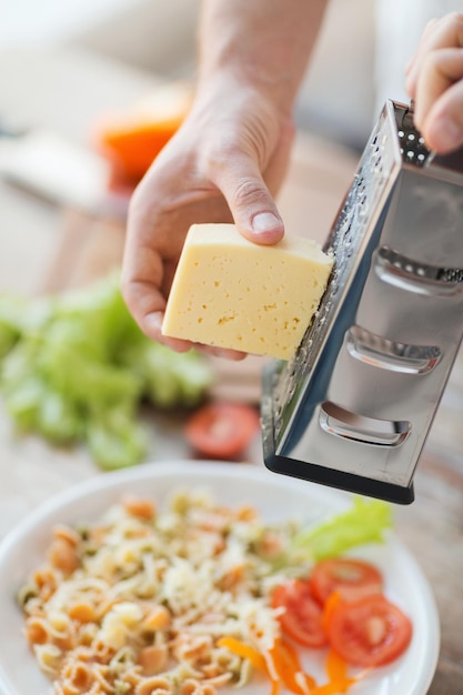 koken, eten en thuisconcept - close-up van mannelijke handen die kaas raspen over pasta