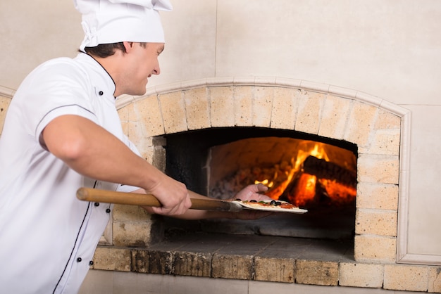 Koken in witte uniform plaatst een gerecht in de oven.