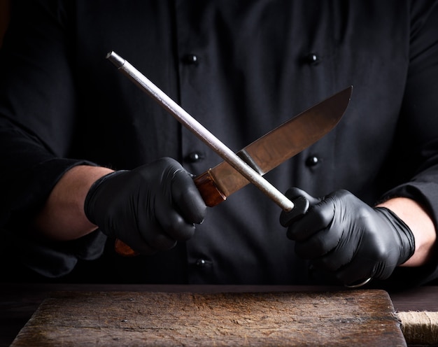 Koken in zwarte latex handschoenen scherpt een mes