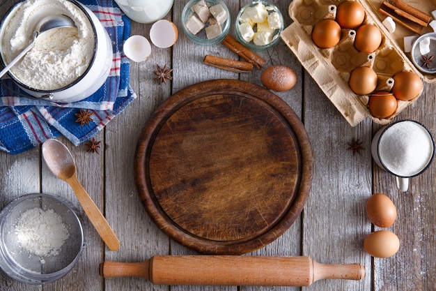 Koken ingrediënten voor het maken van deeg en gebak en houten pizzaplaat op rustiek hout. bovenaanzicht