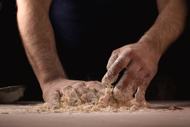 Koken kneeddeeg Mannelijke handen mengen de ingrediënten voor het deeg op tafel tegen een donkere achtergrond