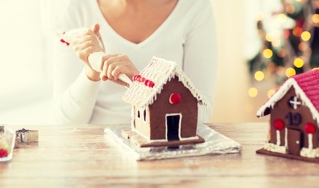 koken, mensen, kerstmis en decoratieconcept - gelukkige vrouw die thuis peperkoekhuizen maakt