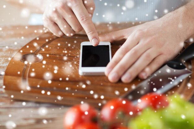 koken, mensen, technologie en thuisconcept - close-up van man leest recept van smartphone en groenten op tafel in de keuken