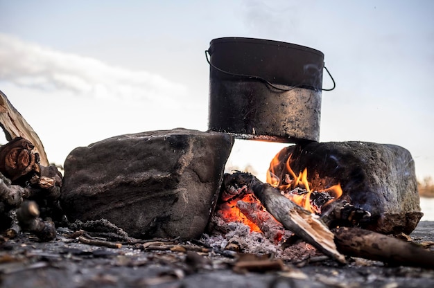 Koken met een bowler die op twee stenen staat en een vuur ertussen, tegen de lucht en de zonsondergang, het vroege voorjaar.