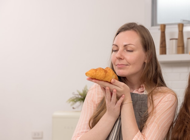 Koken met moeder, gelukkig meisje met dienblad en ruikende vers gekookte croissants, keukeninterieur, kopieerruimte