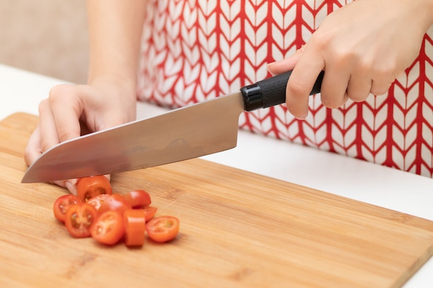 Koken Salade. Vrouwelijke handen snijden cherrytomaten voor Caesar.