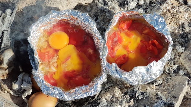 Koken van eieren met tomaten in folie op een vuurtje op het strand