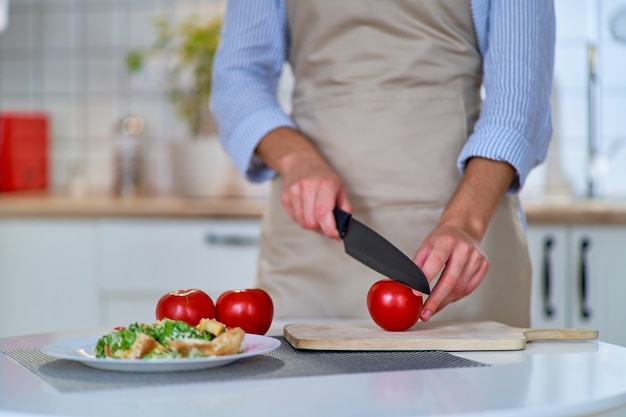 Koken vrouw snijden rijpe verse eco vriendelijke sappige tomaten op een houten bord met behulp van een mes