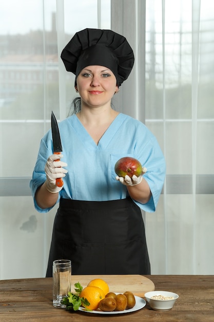 Kokkin houdt in de ene hand een vrucht van mango vast en in de andere hand een mes.