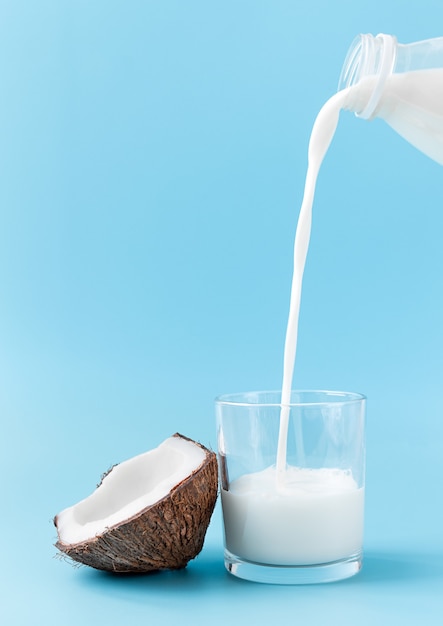 Kokosmelk wordt uit een fles in een glas gegoten. kokos en glas met melk op een blauwe achtergrond.