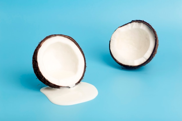 Kokosroom of boter met verse kokosnoten op een blauwe achtergrond. Wit roomsap druipt van kokos.