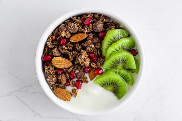 Kom chocolade haver muesli met yoghurt verse kiwi's granaatappel zaden en noten op wit marmeren tafel bovenaanzicht