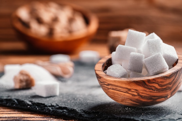 Kom en schep met wit zand en klontjes witte suiker op houten achtergrond Suikerklontje Maak ongezonde voeding obesitas diabetes tandheelkundige zorg en nog veel meer