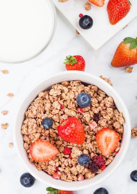 Kom gezonde granen granola met aardbeien en bosbessen en glas melk op marmeren bord