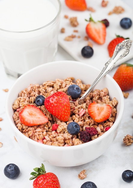 Kom gezonde granen granola met aardbeien en bosbessen en glas melk op marmeren bord