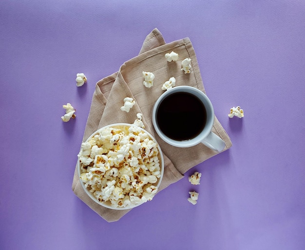 Kom gezouten popcorn met witte mok met drankje op gekleurde achtergrond, bovenaanzicht