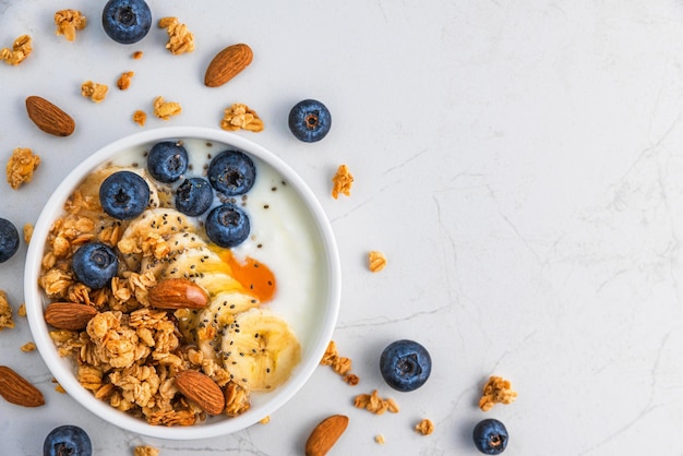 Kom havergranola met yoghurt, banaan, bosbessen, chiazaden en noten op witte achtergrond voor een gezond ontbijt