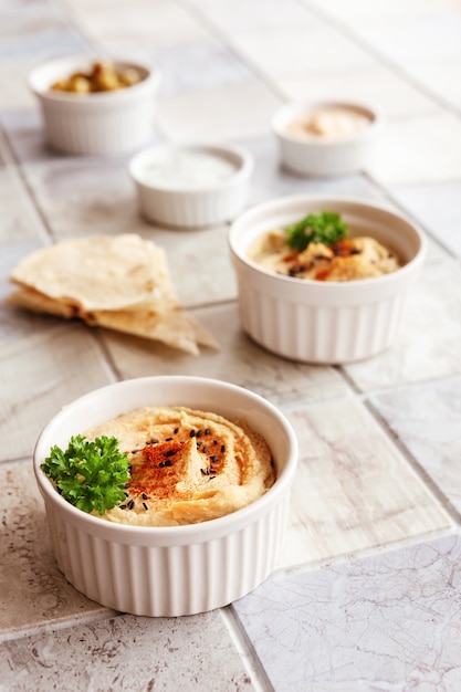 Kom hummus, traditioneel Joods, Arabisch, Midden-Oosters eten van kikkererwten met deeps en met pitabroodje op keramische tegelachtergrond. Close-up, selectieve focus