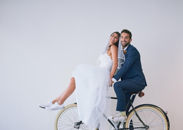 Kom in stijl aan Studio-opname van een pas getrouwd jong stel dat samen op een fiets fietst tegen een grijze achtergrond