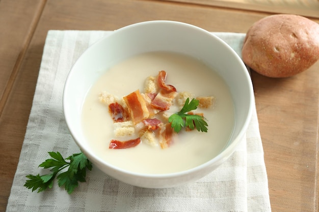 Kom lekkere aardappelsoep met spek op houten tafel