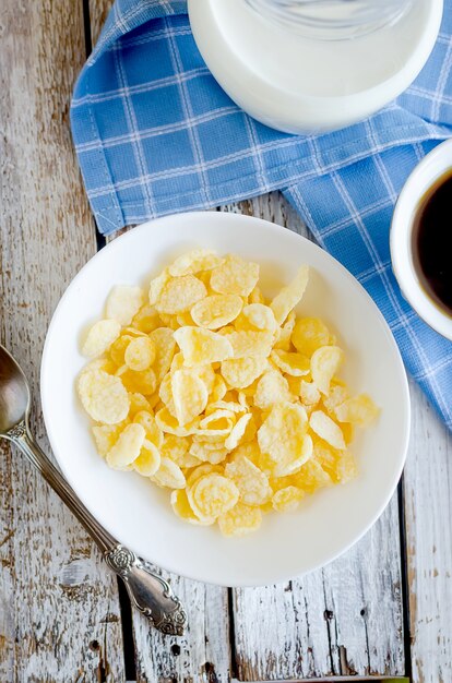 Kom met cornflakes in sugarcoated en lepel, kopje koffie, kruikmelk op tafel